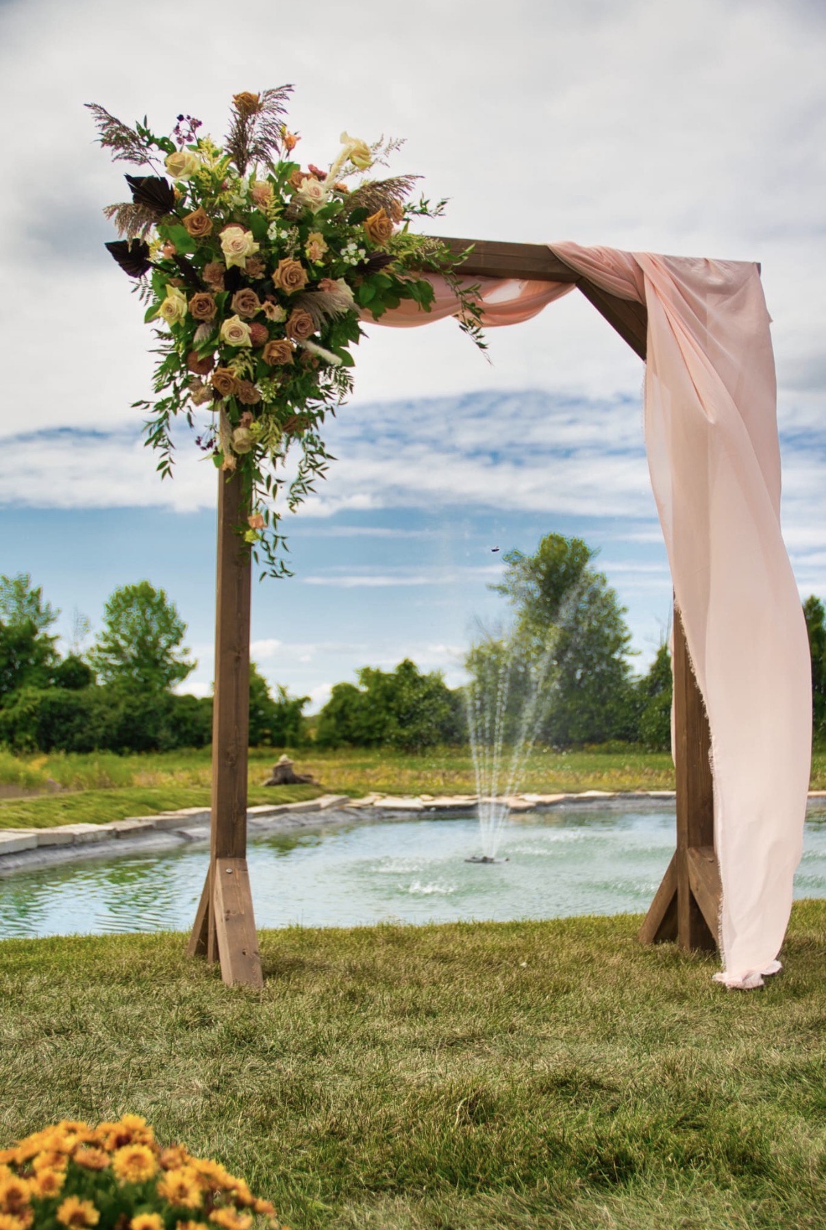 Wooden ceremony arch with blush draping and floral arrangement overlooking the pond and fountain at SV Country Estate