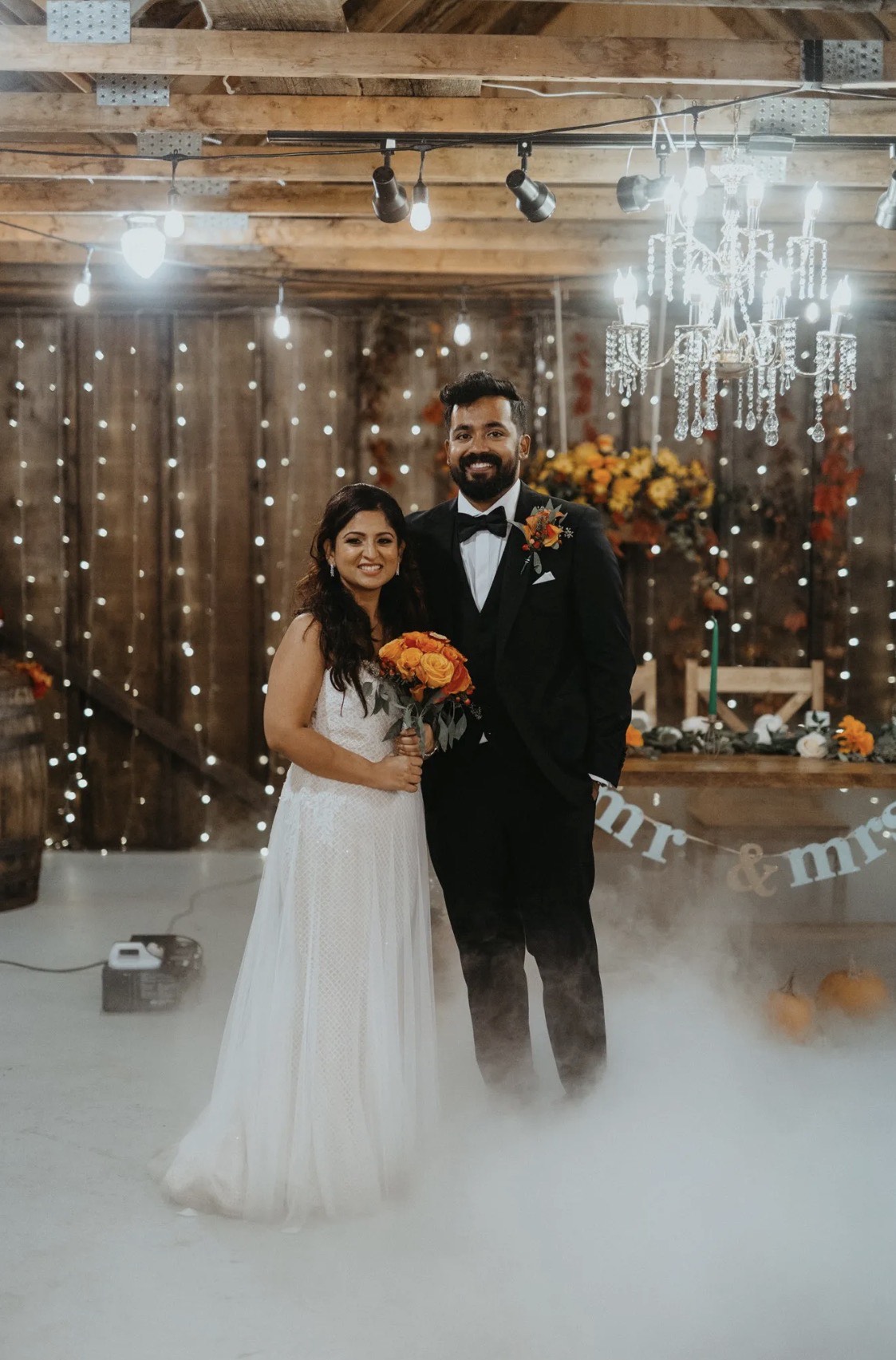 Bride and groom under crystal chandeliers in the barn with autumn florals