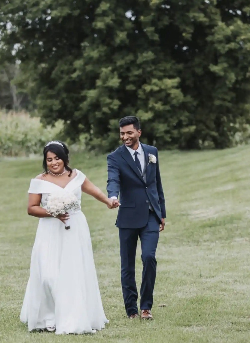 Bride and groom walking hand in hand across the open lawn