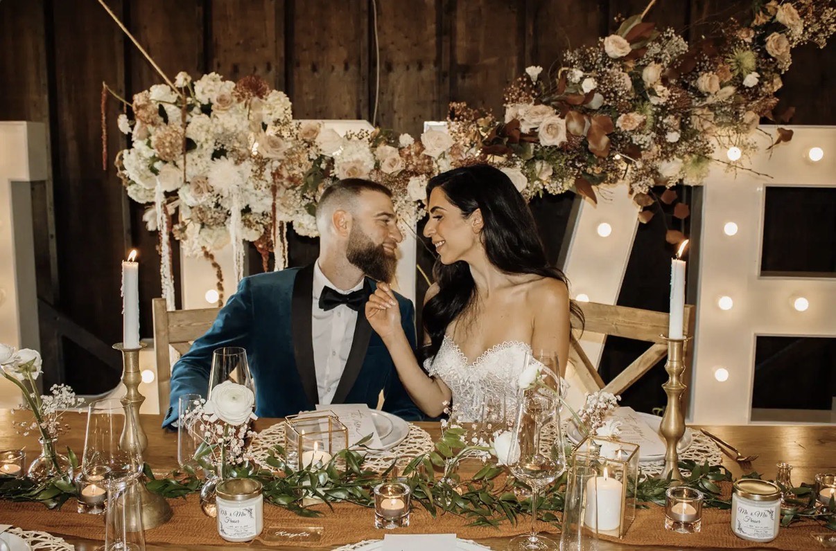 Newlyweds at a candlelit sweetheart table inside the timber-frame barn